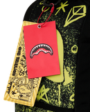 Close-up of a black Sprayground backpack with a neon yellow graphic print, featuring a bright red hangtag with a shark-mouth logo and a yellow patterned paper tag.