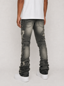 Rear view of a person wearing heavily distressed dark gray washed jeans with ripped details and cuffed hems, paired with a white t-shirt and white platform sneakers, against a light gray studio background.