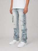 A person wearing light-wash blue cargo-style jeans with multiple flap pockets and distressed details, paired with a white t-shirt and white sneakers, against a light gray studio background.
