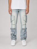 A person wearing light-wash blue cargo jeans with large flap pockets on the thighs and lower legs, paired with a white t-shirt and white sneakers, photographed against a light gray studio background.