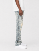 A person shown from the waist down wearing light-wash distressed jeans with a faded marble or mineral-wash pattern and ripped details, paired with a white t-shirt and white sneakers, against a plain light gray studio background.