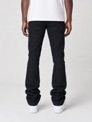 Rear view of a person wearing black flared jeans with a white t-shirt and white sneakers, photographed against a light gray studio background.