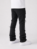Ripped black denim jeans with frayed details and tassel accents, shown on a model from the back wearing a white t-shirt and white sneakers against a light gray background.