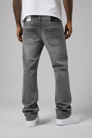 Rear view of a person wearing gray washed denim jeans, a white t-shirt, and white sneakers against a light gray studio background.