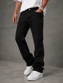 A person wearing black straight-leg jeans, a white t-shirt, and white sneakers, standing against a textured gray concrete wall.