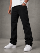 A person wearing black straight-leg jeans with white sneakers and a white t-shirt, standing against a gray concrete wall.