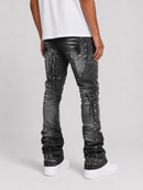 Rear view of a person wearing heavily distressed black denim jeans with silver studs and decorative stitching, paired with a white t-shirt and white sneakers, on a light gray studio background.