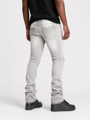 A person shown from the back wearing light gray washed skinny jeans with frayed, distressed detailing running down the outer sides of the legs, paired with a black t-shirt and black shoes, against a plain white studio background.