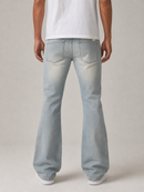 A person shown from the back wearing light-wash blue jeans with a white t-shirt and white sneakers, photographed against a plain light gray studio background.